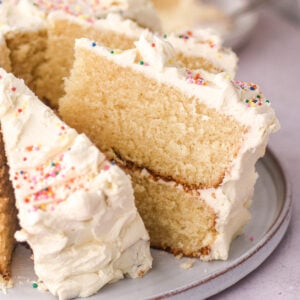 Vanilla buttercream cake shown sliced. You can see one slice up close and the fluffy texture of the vanilla cake.