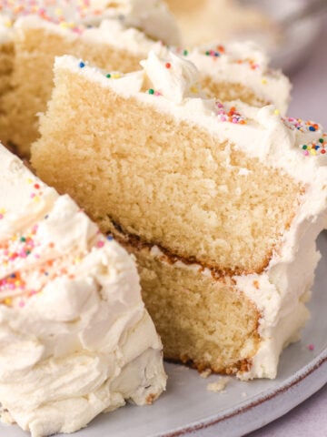 Vanilla buttercream cake shown sliced. You can see one slice up close and the fluffy texture of the vanilla cake.
