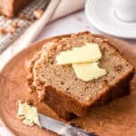 A slice of banana bread on a white plate with butter on top of it.