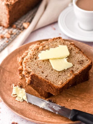 A slice of banana bread on a white plate with butter on top of it.