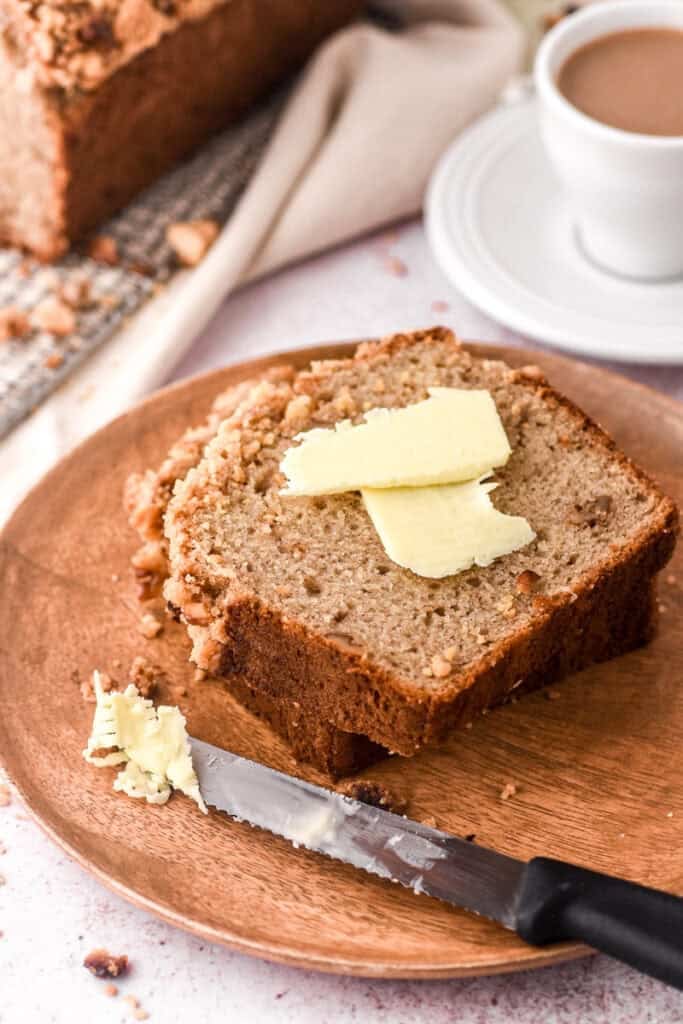 A slice of banana bread on a white plate with butter on top of it.