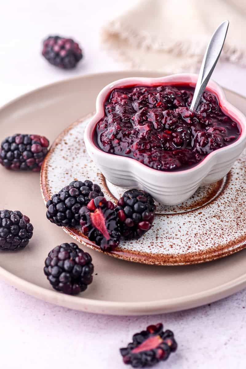 Blackberry Compote shown in a small fluted bowl next to fresh blackberries. 