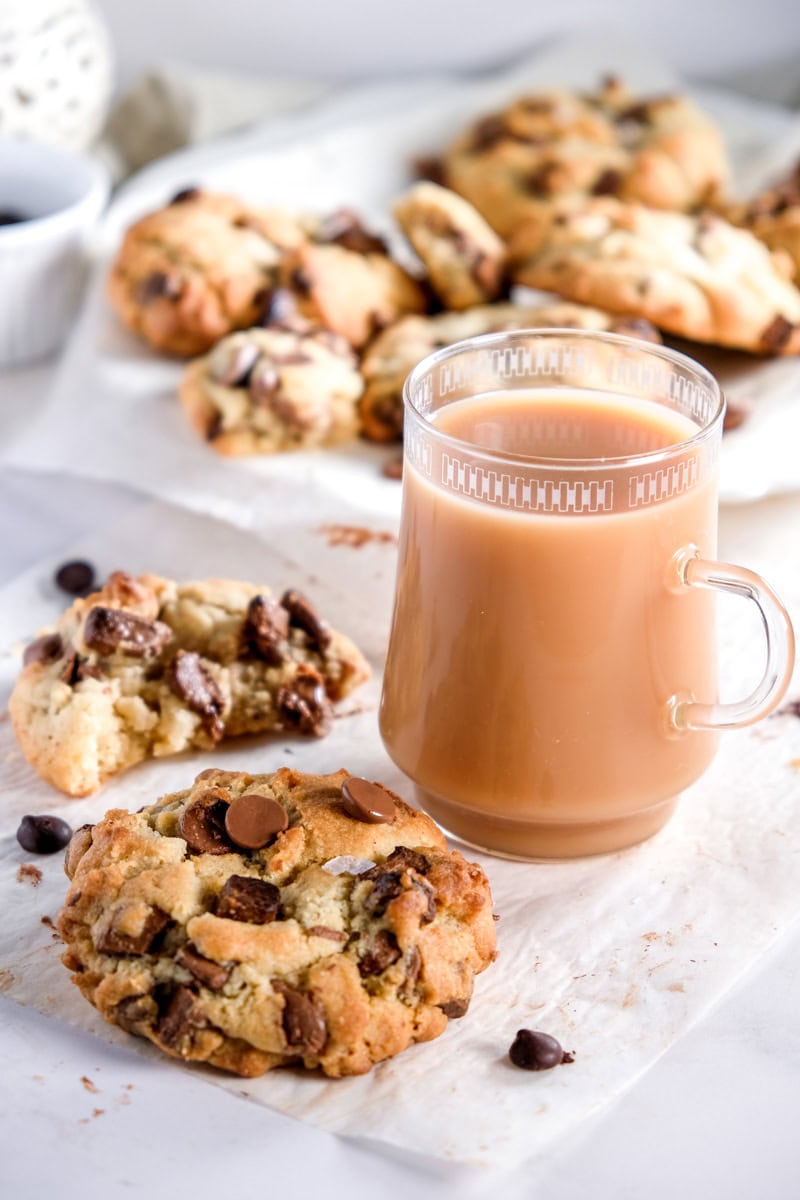 Milk Chocolate Cookie shown next to a mug of tea, there are more cookies on a plate in the background.
