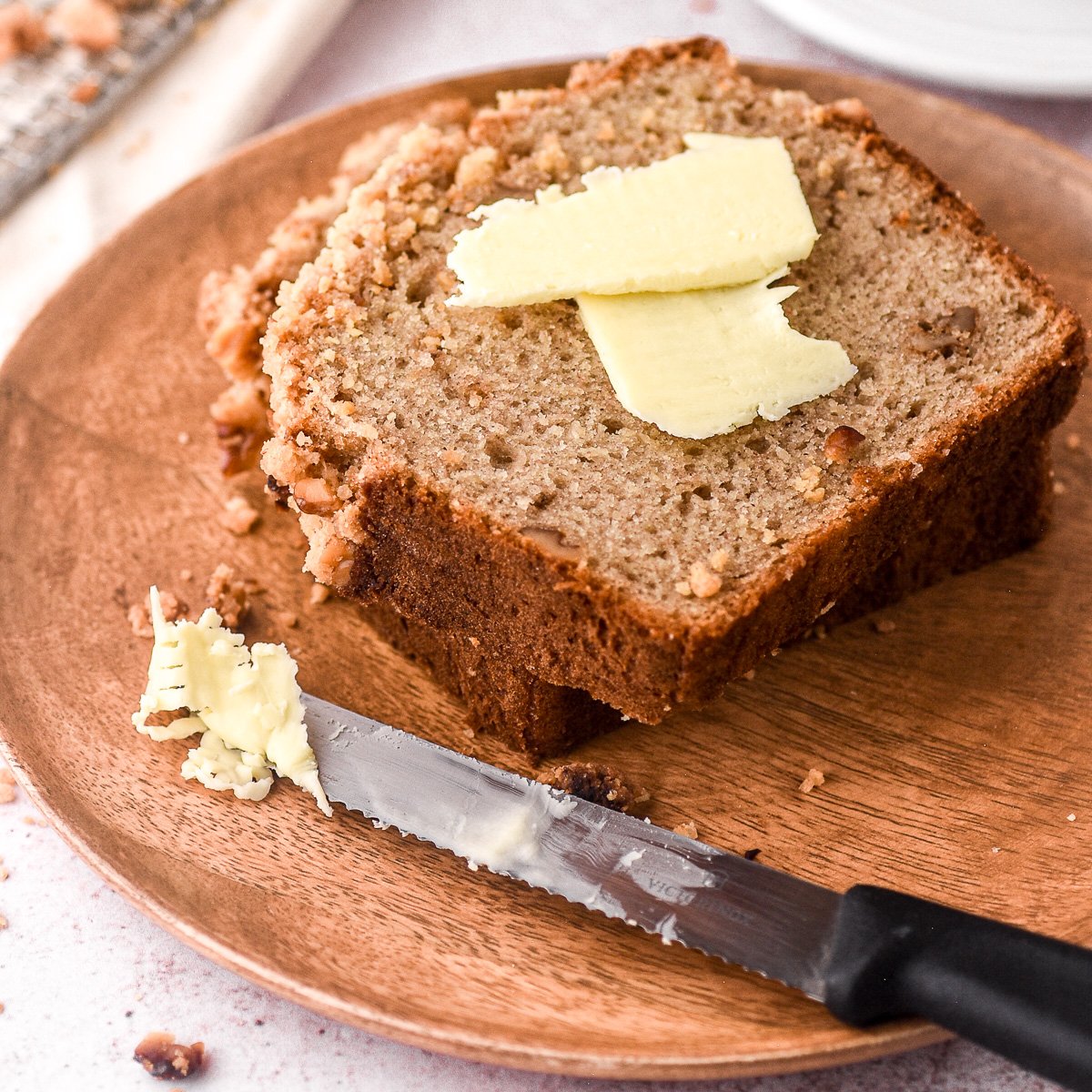 A slice of banana bread shown on a wooden plate with butter.