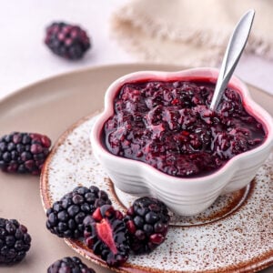 Image shows blackberry compote for desserts and cakes shown in a small bowl next to fresh blackberries.