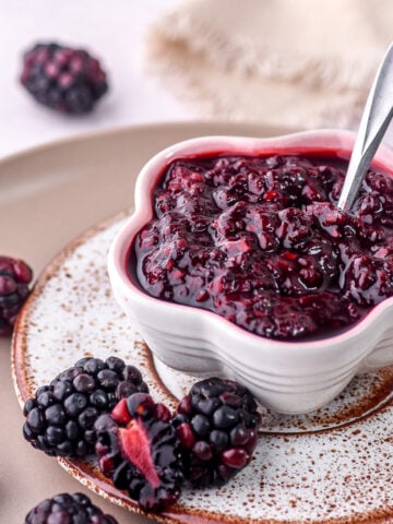 Image shows blackberry compote for desserts and cakes shown in a small bowl next to fresh blackberries.