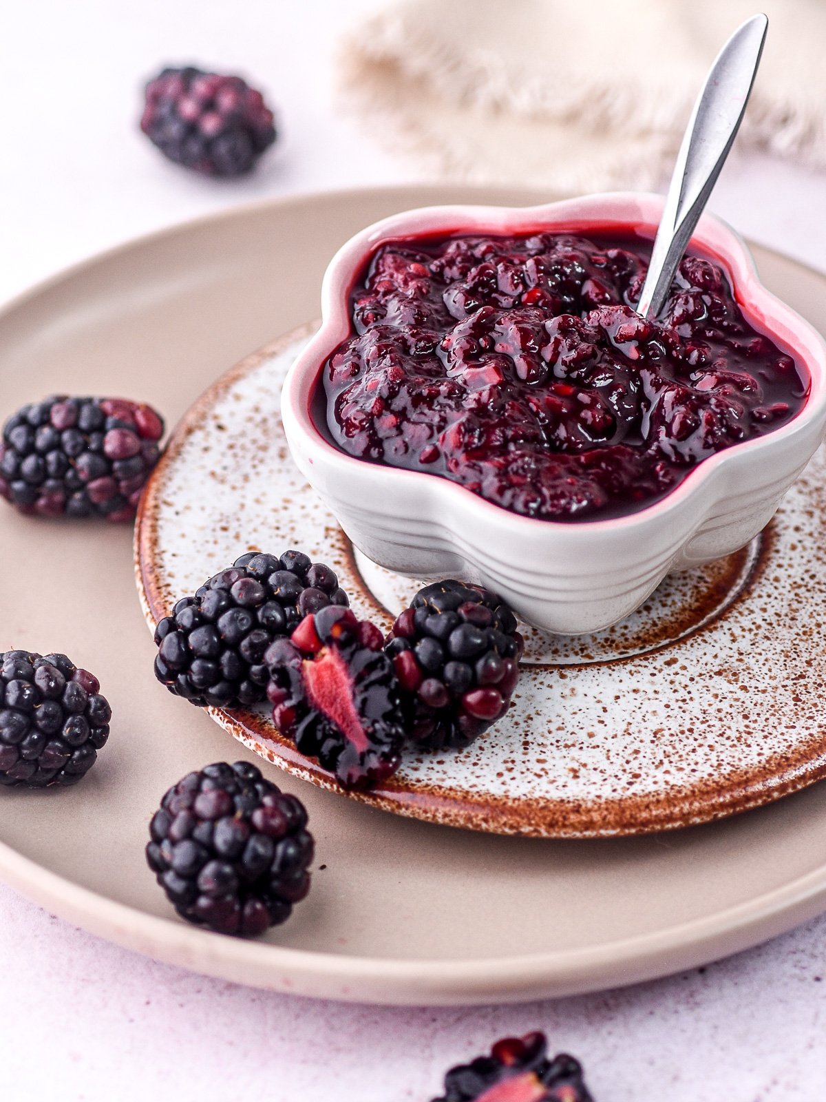 Blackberry Compote shown in a small fluted bowl next to fresh blackberries.