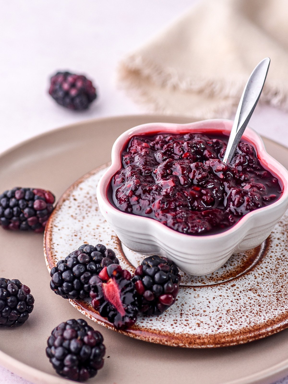 Blackberry compote for cake and cupcake fillings show in a small white bowl next to fresh blackberries.