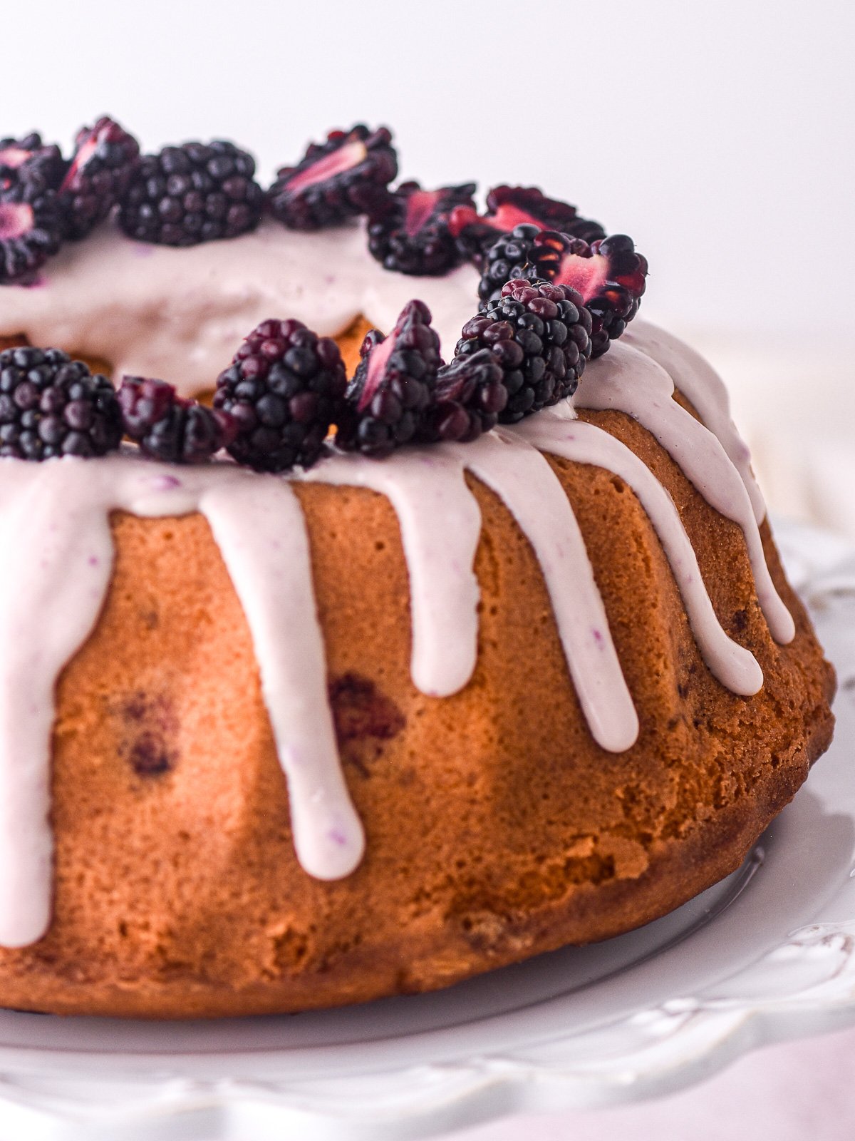 Image shows the bundt cake from the side, you can see the blackberry and white chocolate drip dripping down the cake.