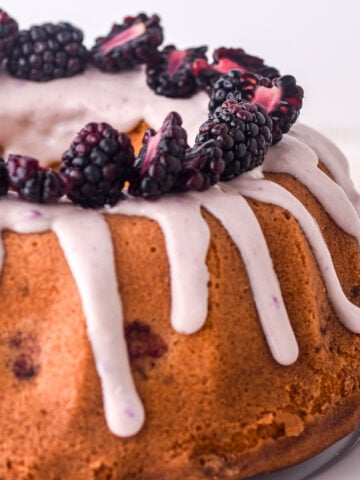 Lemon blackberry bundt cake shown from a side angle, you can see the white chocolate blackberry drip coming down the sides of the cake.