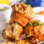 Image shows a pile of muffins on a plate, there is a blue coffee cup in the background.