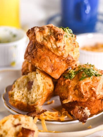 Image shows a pile of muffins on a plate, there is a blue coffee cup in the background.
