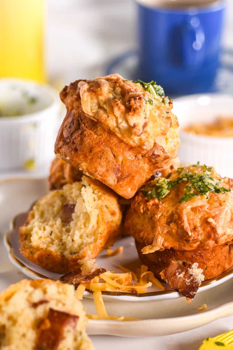 A pile of muffins shown on a plate, there is a blue coffee cup in the background.