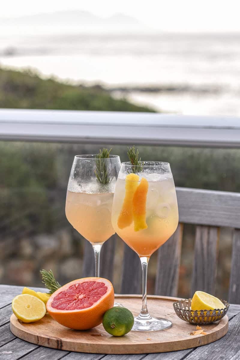 Image shows two cocktails on a balcony with the sea in the background. 