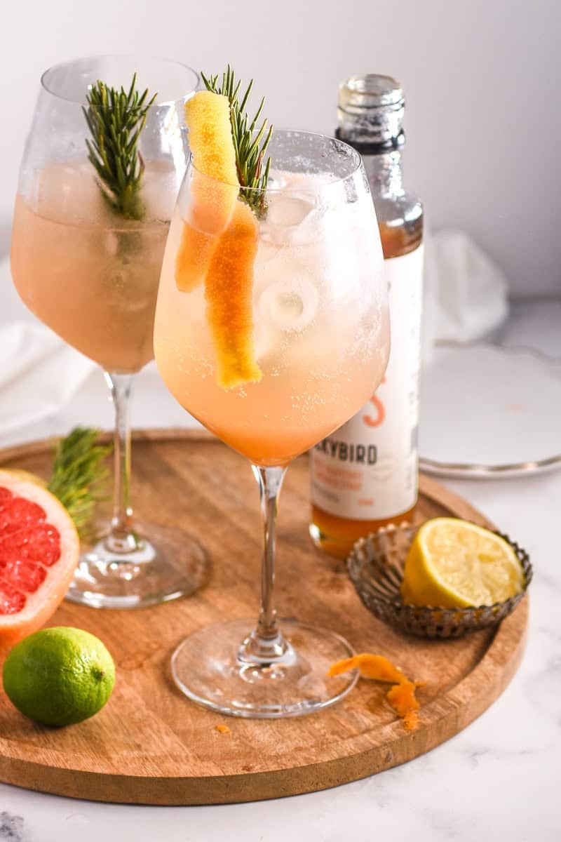Image shows two glasses filled with the cocktail on a wooden board next to fresh citrus. 