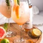 Gin spritz cocktail shown on a round wooden plate next to various citrus fruits.