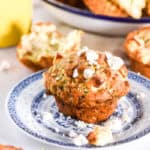 Zucchini and feta muffin shown on a blue plate, there are other muffins in the background.