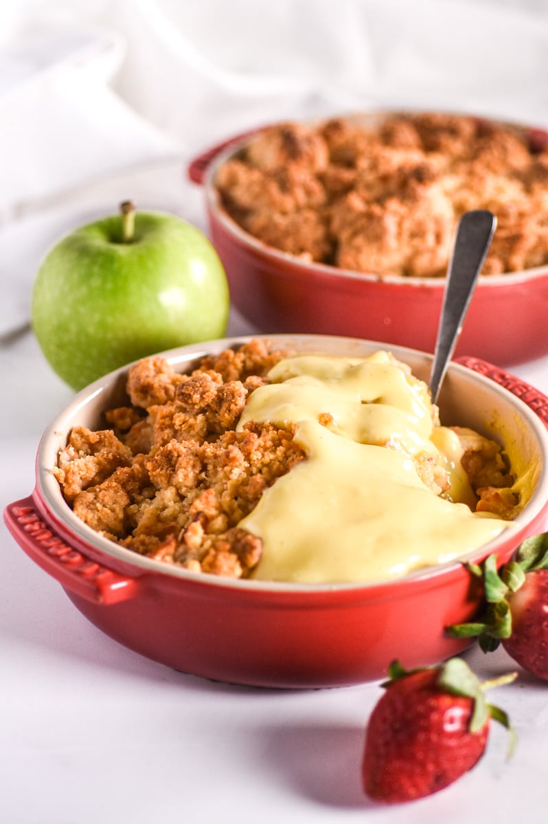 Image shows two dishes filled with the baked crumble, custard has been poured over the one. 