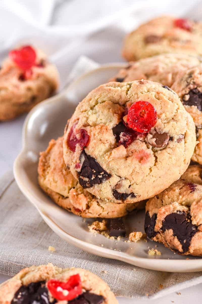 Image showing the cookies piled on a plate, you can see the chunks of chocolate and pieces of red glacé cherries. 