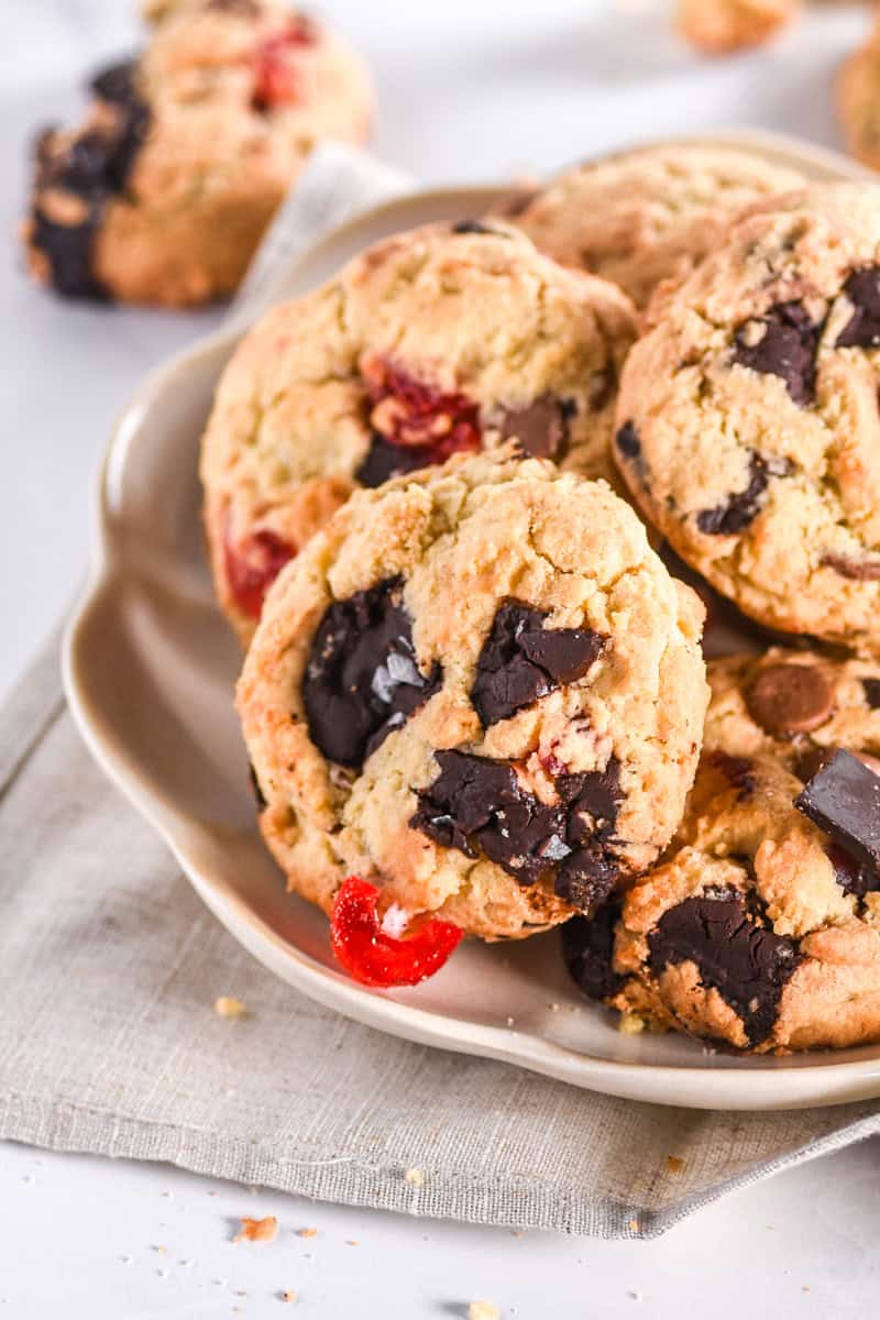 Image showing cookies on a plate, you can see the pools of dark chocolate , milk chocolate and the flecks of cherry pieces. 
