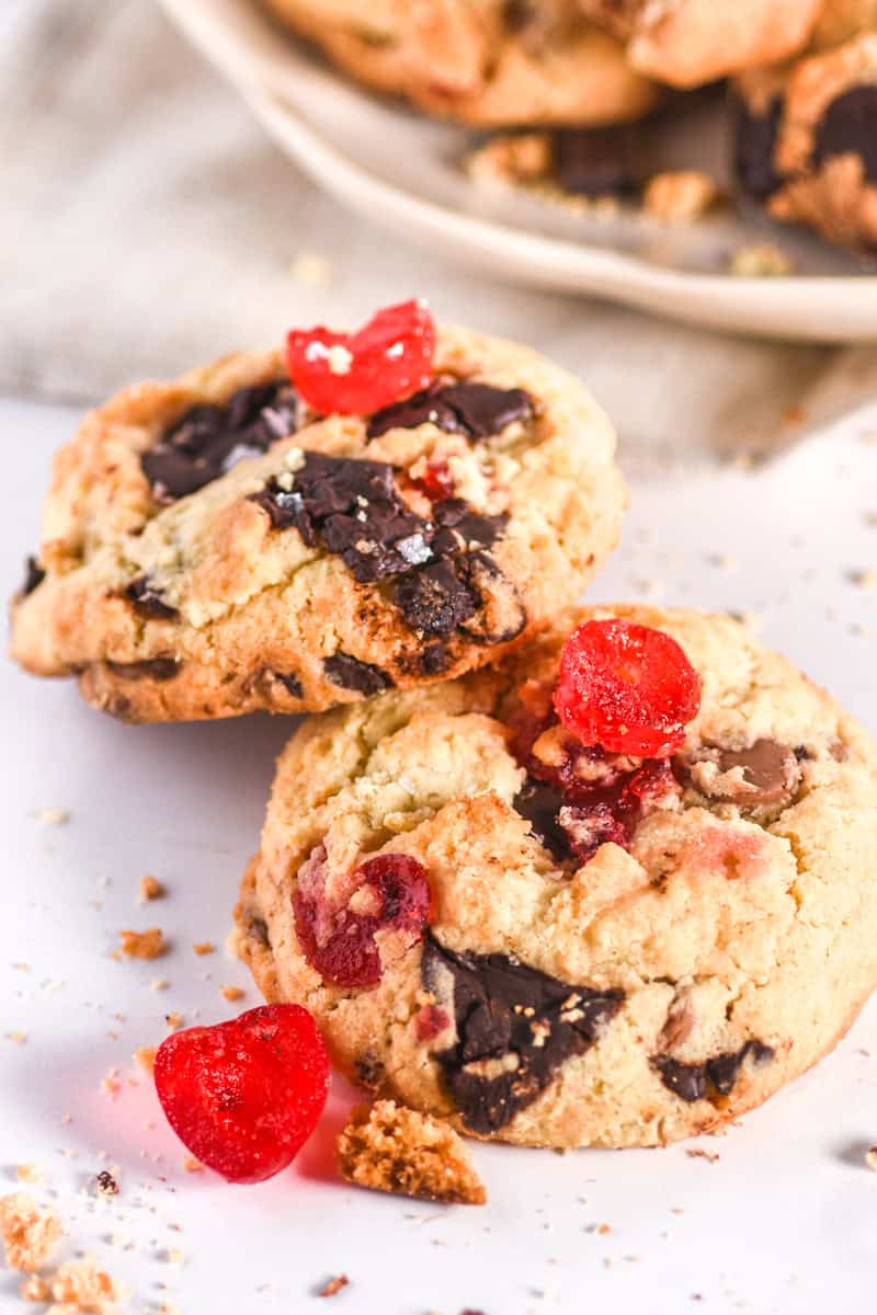 Image showing two cookies on a counter there are crumbs and cherries scattered around the cookies. 