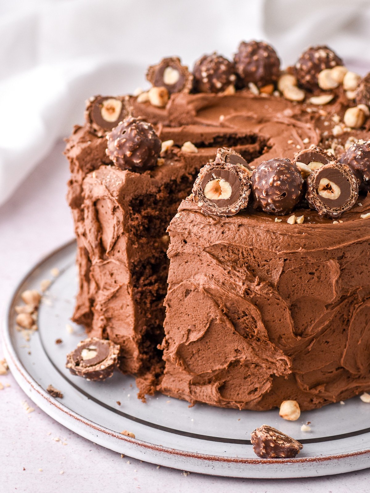 Chocolate Nutella Ferrero Rocher Cake shown decorated with whole and sliced Ferreo Rocher chocolates and toasted hazelnuts.