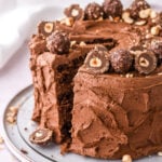 Chocolate Nutella Ferrero Rocher cake shown on a cake plate with a few slices cut.