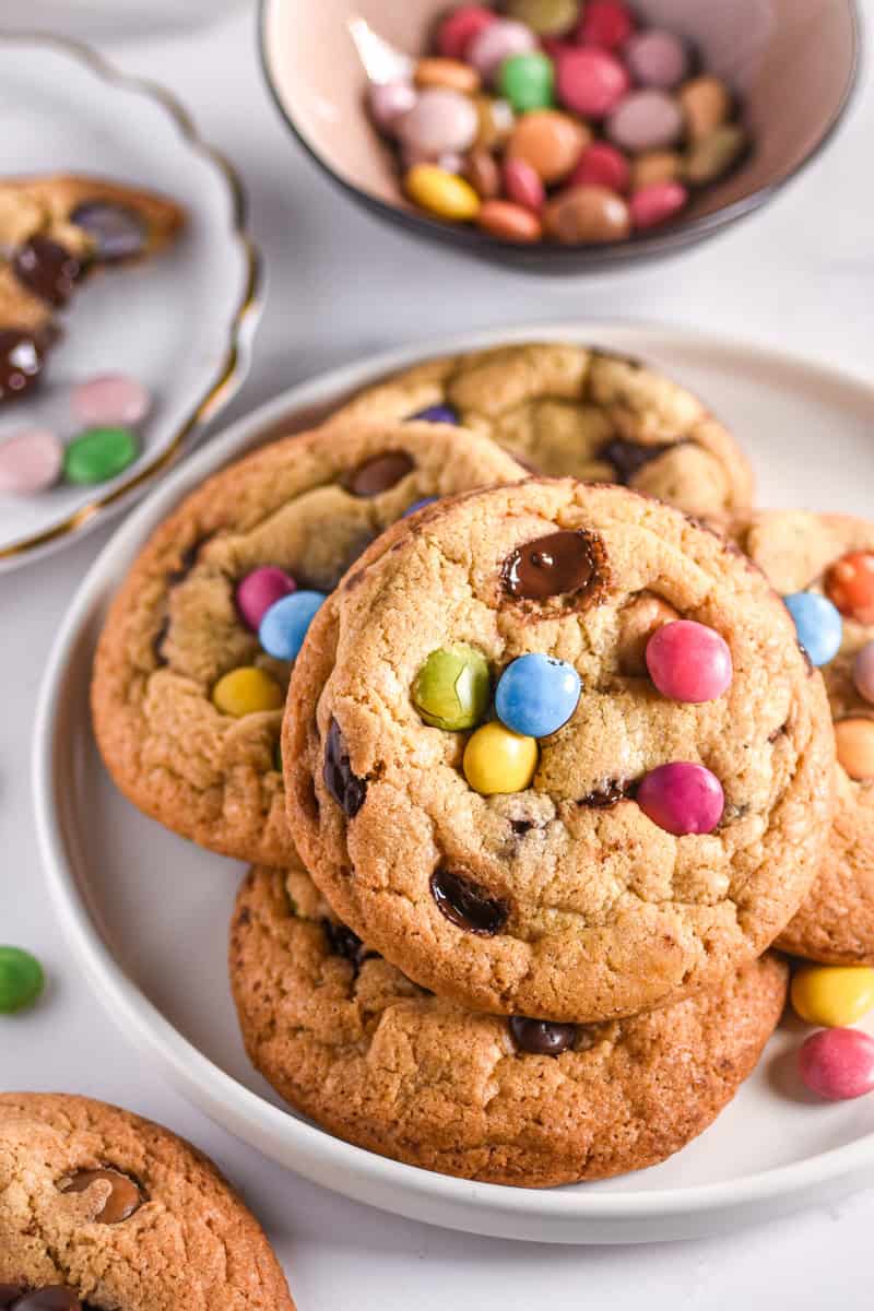 Smarties Cookies shown on a white plate, there is a bowl of smarties in the background. 