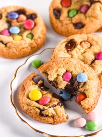 Smarties Cookies shown on a white plate, the cookie in the front is broken in half.