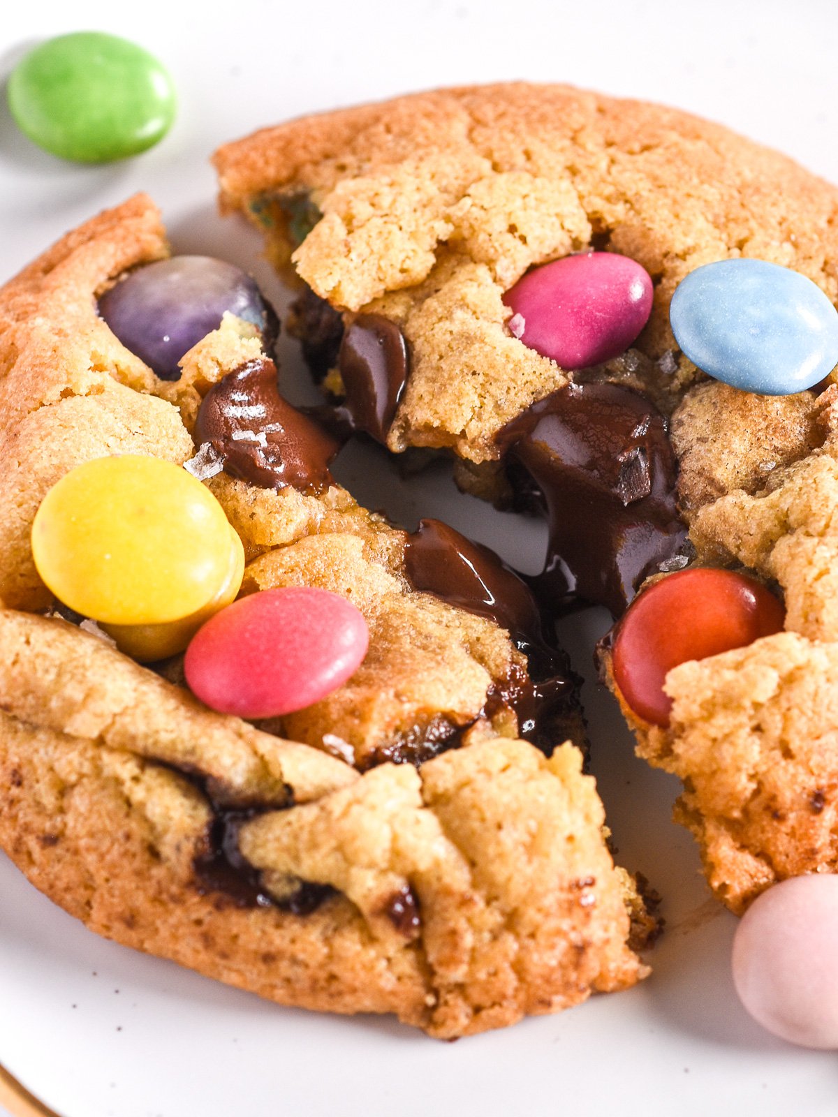 Smarties Cookie shown up close and broek in half so can se the melted chocolate oozing out of the cookie. 