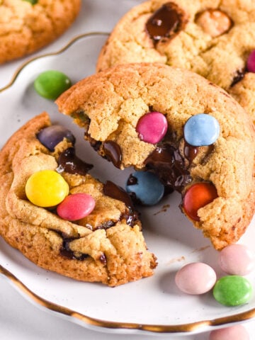 Smarties cookies shown on a white plate with smarties scattered around.