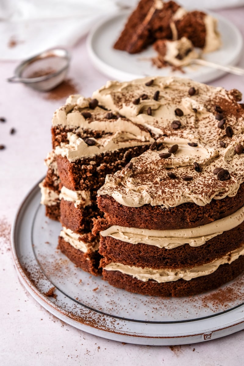 Chocolate Espresso Layer Cake shown with slices cut on a kitchen counter next to coffee beans and dusted cocoa. 