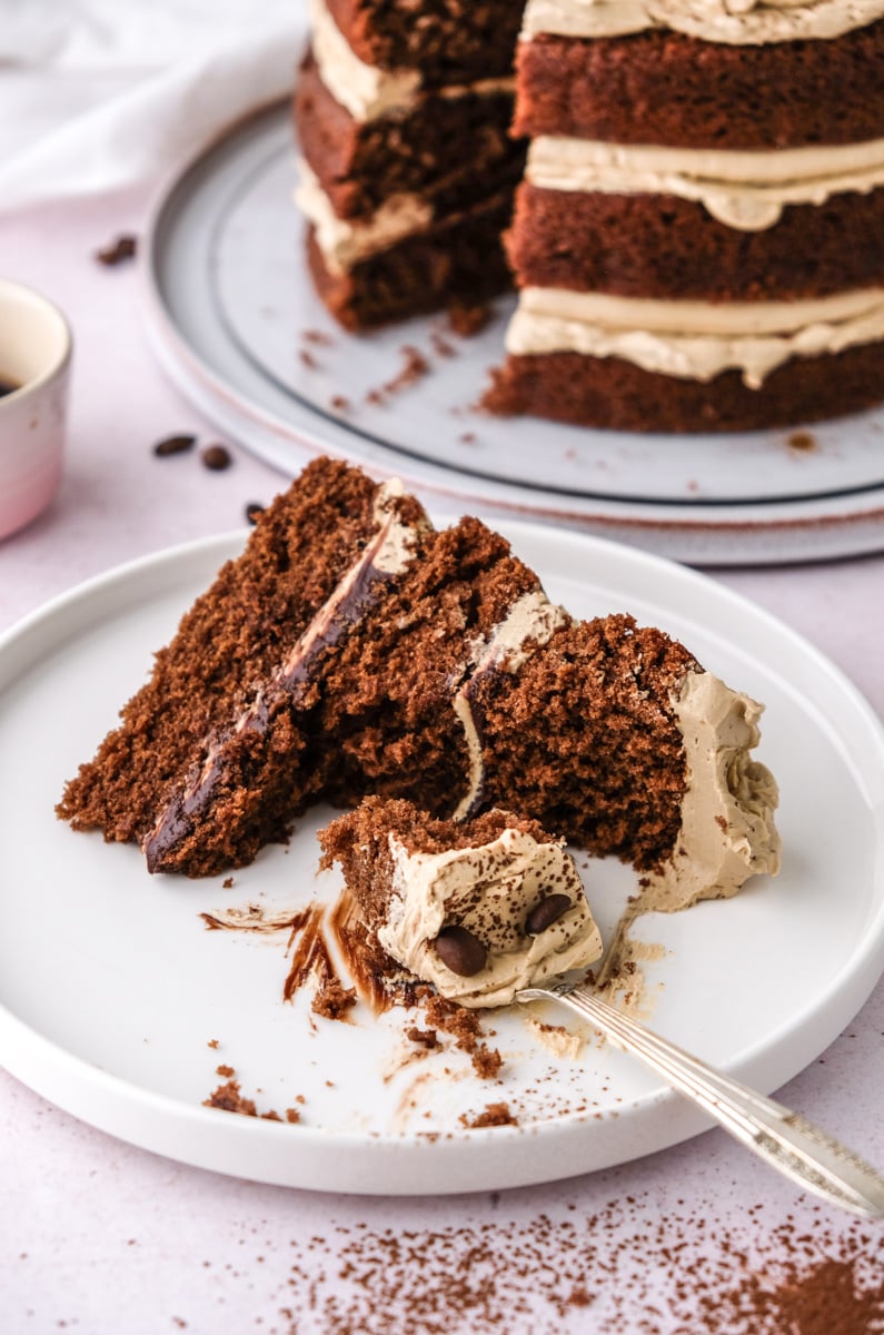 A half eaten slice of coffee espresso cake shown on a white plate with a fork. 