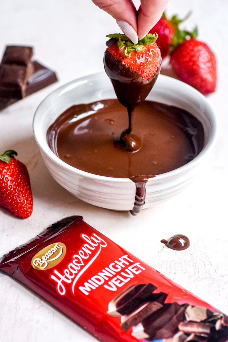 Image shows a strawberry being dipped into melted chocolate.