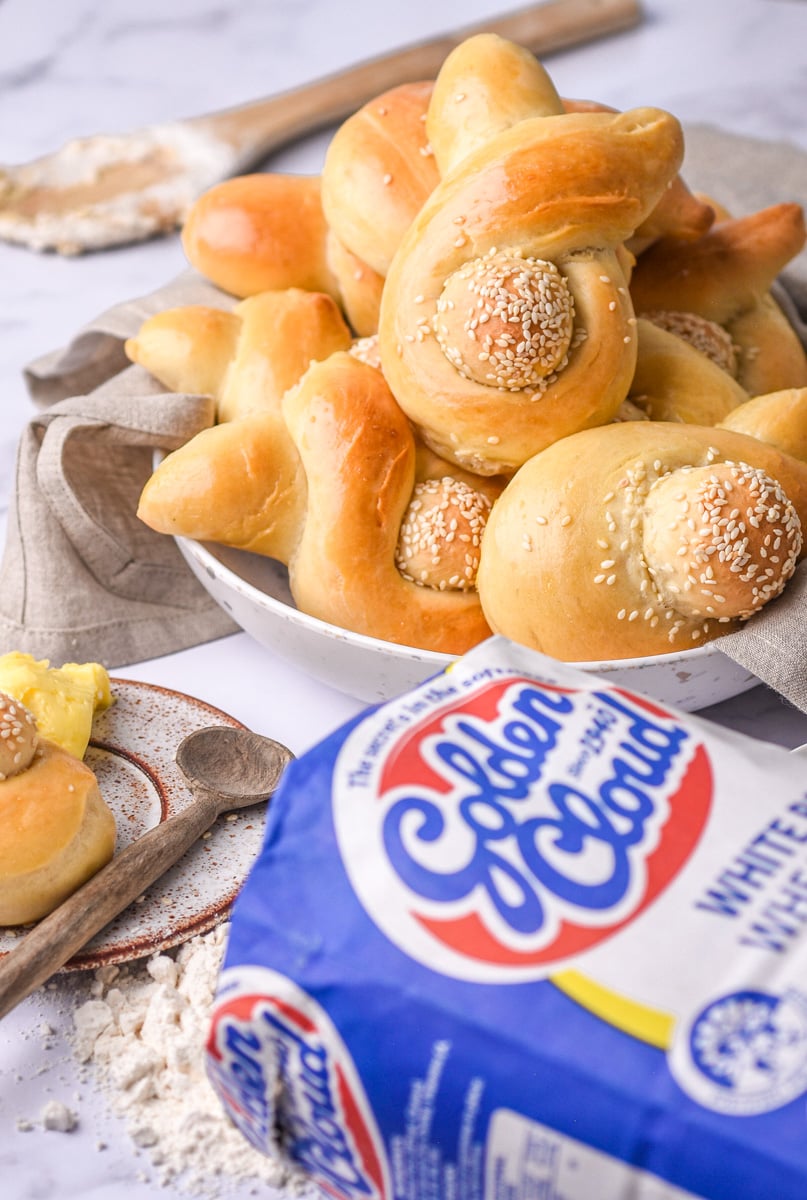 Image shows bunny shaped bread rolls in a bowl and a bag of flour in front of them.