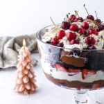 Black Forest Trifle shown in a glass stand dish. There is a Christmas tree candle in the background.