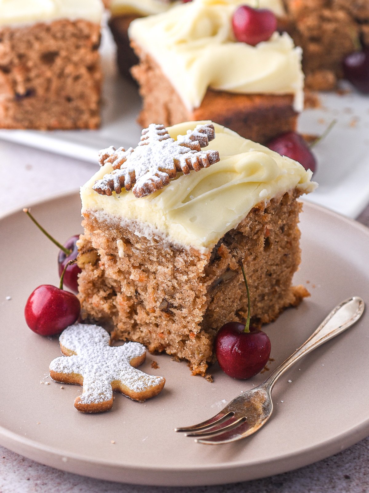 Christmas Carrot Sheet Cake slice shown on a plate, there are fresh cherries scattered around the plate. 