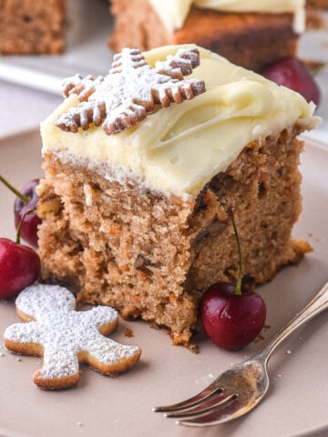 A slice of Christmas carrot sheet cake shown on a plate next to a fork.