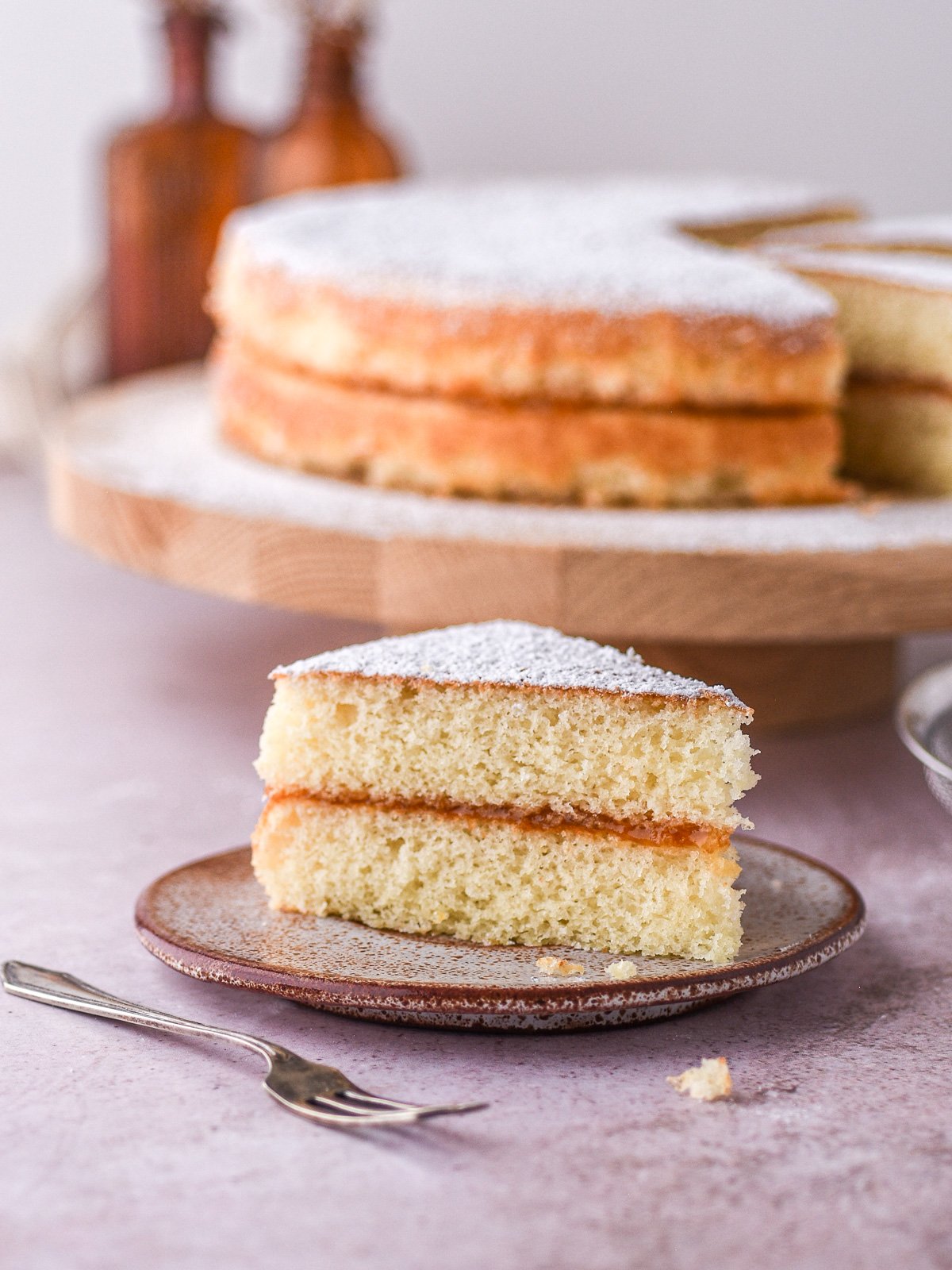 Image showing a slice of simple birthday cake on a plate with the whole cake in the background.