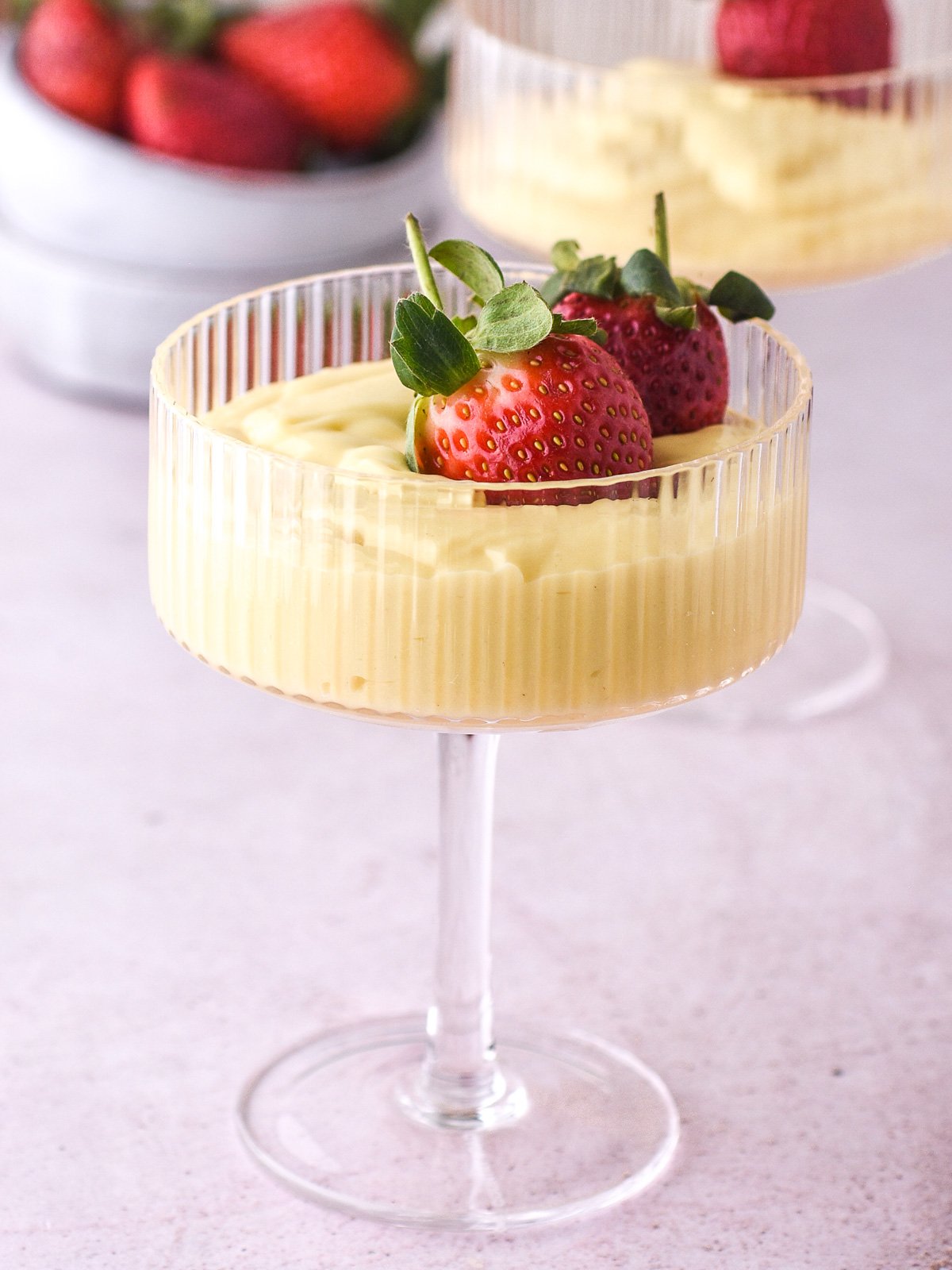 Image shows a tall cocktail glass filled with custard and decorated with fresh strawberries.