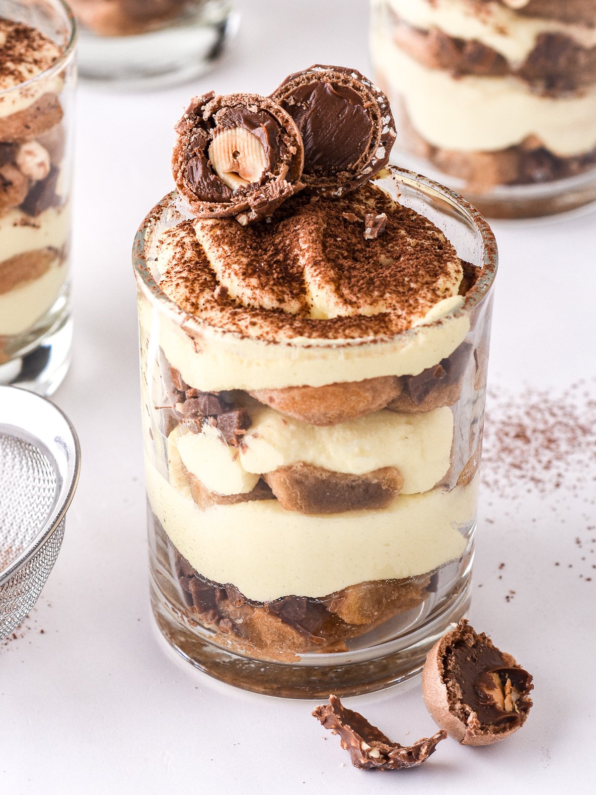 Image shows a individual glass filled with tiramisu and topped with a halved ferrero rocher.