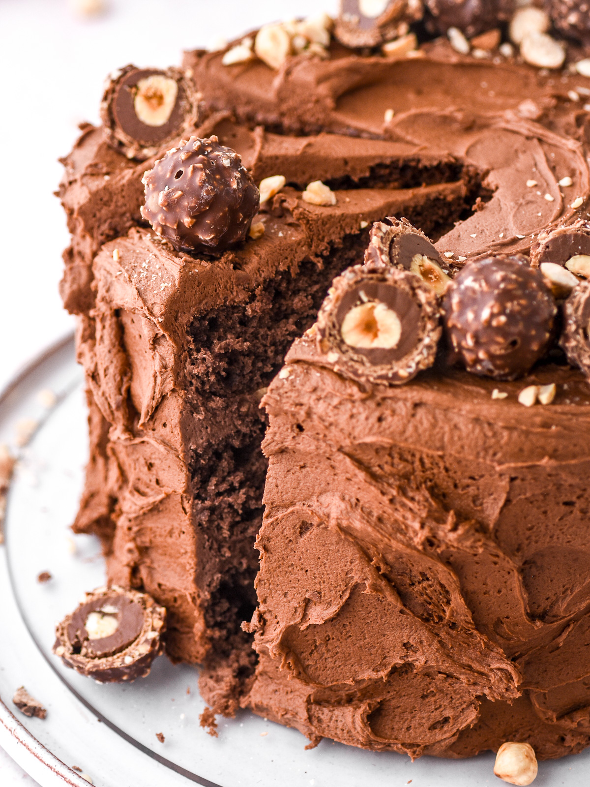 Image showing a ferrero rocher cake with some slices cake, the cake is decorated with hazelnuts and chopped ferrero rocher chocolates.