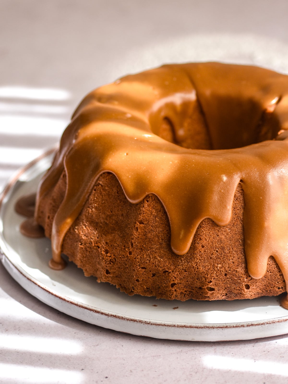 Apple Pecan Cake with caramel glaze shown on a cake plate. Thick drip of sauce are falling down the sides of the cake.