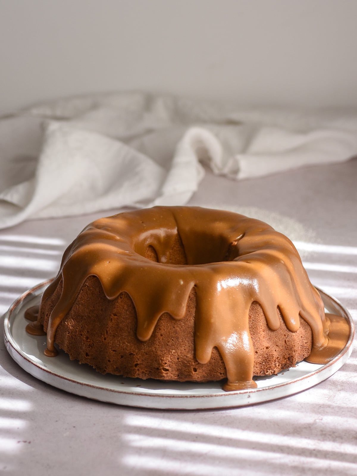 Apple Pecan Bundt Cake covered in caramel glaze. the glaze is dripping down the sides of the cake.