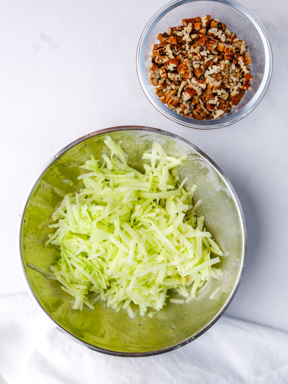 Image shows step 1 of how to make an apple and pecan cake: grate apples and chop pecans.