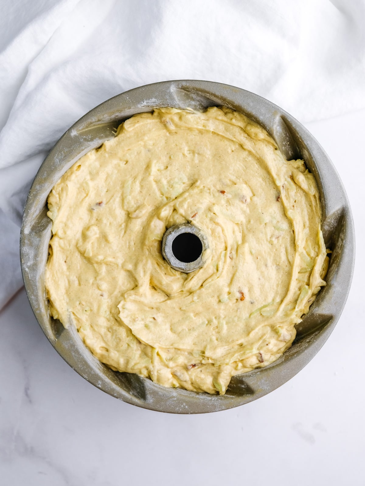 Image shows step 7 of how to make an apple and pecan cake: pour into bundt cake pan and bake.