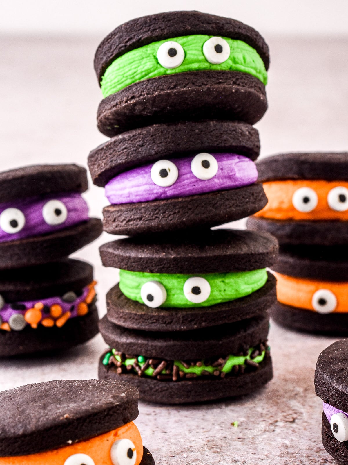 Chocolate Halloween Monster Cookie Sandwiches filled with different coloured buttercream shown on a kitchen counter.