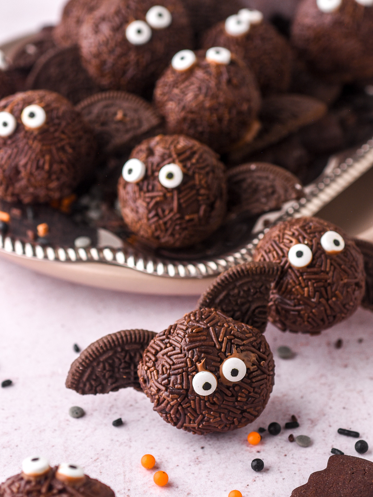 No-Bake Chocolate Halloween Truffles decorated with edible eyes and Oreo bat wings shown on a silver tray.