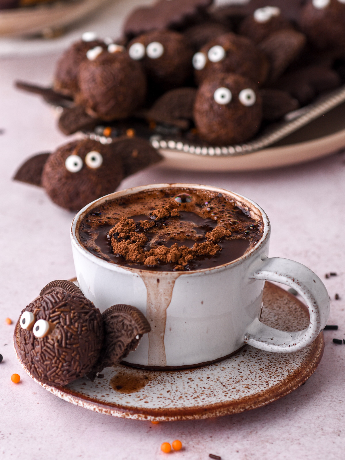 No-Bake Chocolate Halloween Truffle shown next to a cup of hot chocolate. There are more truffles in the background.