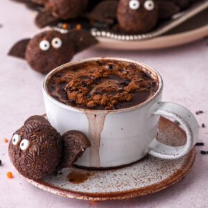 No-Bake Chocolate Halloween Truffle shown next to a cup of hot chocolate. There are more truffles in the background.